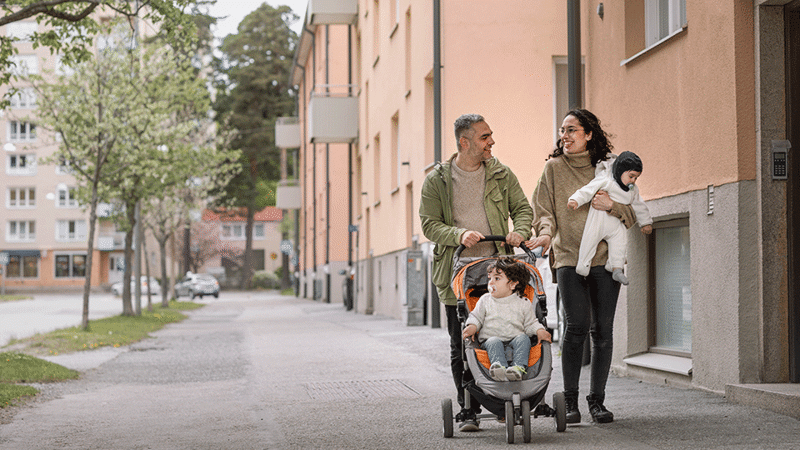 Familj går med barnvagn och hund längs bostadsgata.
