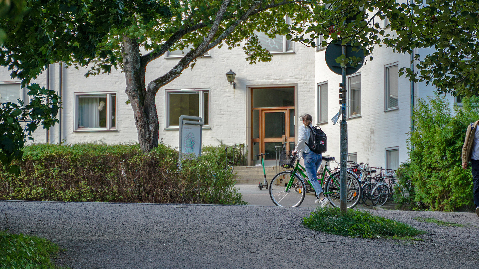 Cykel parkerad utanför bostadsentré i lummig miljö.